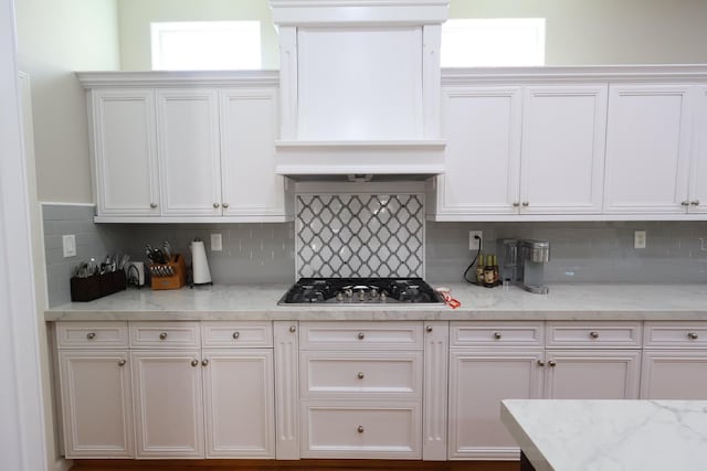 2143 Everglade Ave, Clovis, CA 93619 - kitchen featuring stainless steel gas cooktop, custom range hood, white cabinets, decorative backsplash, and light stone countertops