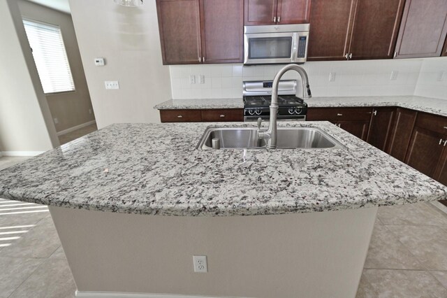 3368 Monterosa Ln, Clovis, CA 93619 - kitchen with stainless steel appliances, light stone counters, backsplash, a center island with sink, and baseboards