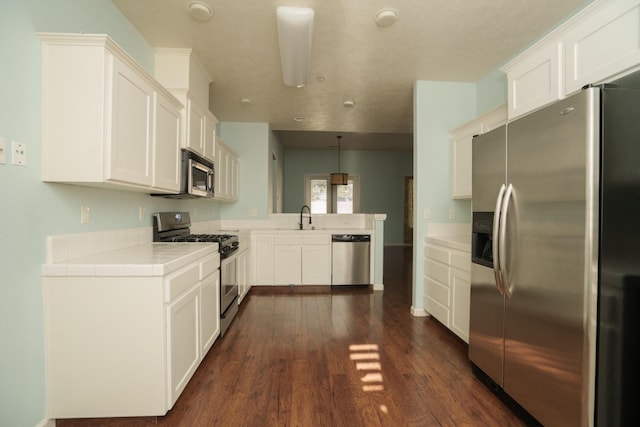 5138 W Beechwood Ave, Fresno, CA 93722 - kitchen with appliances with stainless steel finishes, a peninsula, tile countertops, dark wood finished floors, and white cabinets