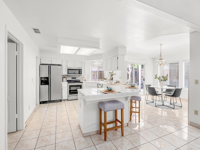 7549 N 8th, Fresno, CA 93720 - kitchen with stainless steel appliances, tile counters, a peninsula, and light tile patterned flooring