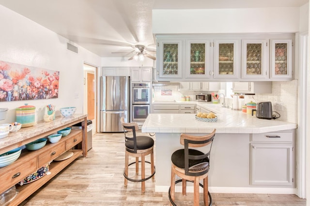 2934 N 8th St, Fresno, CA 93703 - kitchen with stainless steel appliances, a peninsula, a breakfast bar, a sink, and glass insert cabinets