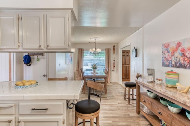 2934 N 8th St, Fresno, CA 93703 - kitchen with tile counters, light wood-type flooring, a chandelier, white cabinetry, and a textured ceiling