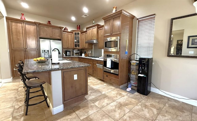 3257 Twain Ave, Clovis, CA 93619 - kitchen with stainless steel appliances, a sink, brown cabinetry, dark stone counters, and glass insert cabinets