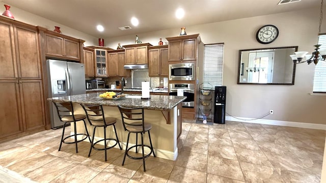 3257 Twain Ave, Clovis, CA 93619 - kitchen with appliances with stainless steel finishes, under cabinet range hood, brown cabinets, a center island with sink, and tasteful backsplash