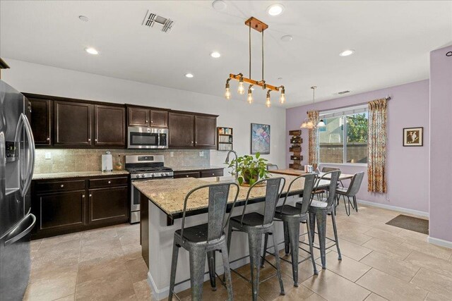3930 Saginaw Ave, Clovis, CA 93619 - kitchen featuring appliances with stainless steel finishes, backsplash, light stone counters, a kitchen breakfast bar, and a center island with sink