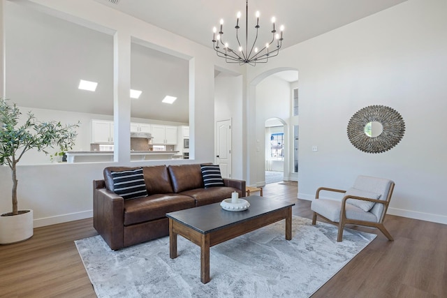 5642 W Beechwood Ave, Fresno, CA 93722 - living area featuring arched walkways, light wood finished floors, baseboards, a high ceiling, and a chandelier