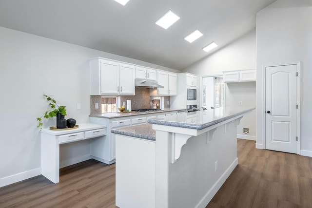 5642 W Beechwood Ave, Fresno, CA 93722 - kitchen with wood finished floors, white cabinets, decorative backsplash, under cabinet range hood, and high vaulted ceiling