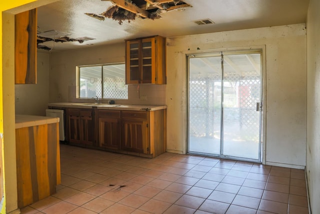 1315 W Fedora Ave, Fresno, CA 93705 - kitchen featuring dishwasher, light tile patterned floors, glass insert cabinets, tile counters, and brown cabinetry