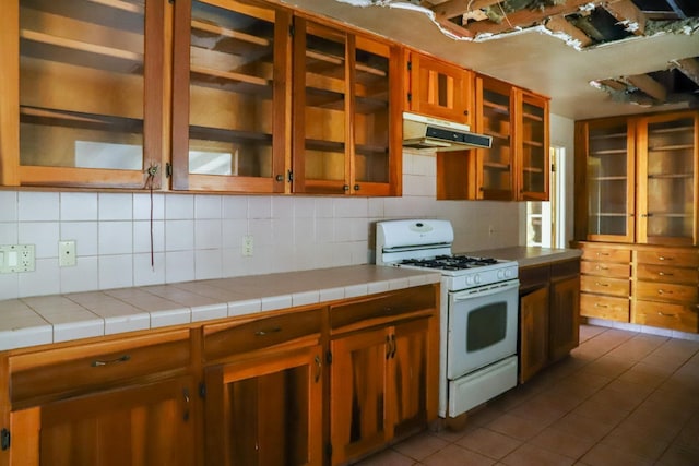 1315 W Fedora Ave, Fresno, CA 93705 - kitchen with white range with gas stovetop, under cabinet range hood, tasteful backsplash, dark tile patterned floors, and brown cabinetry
