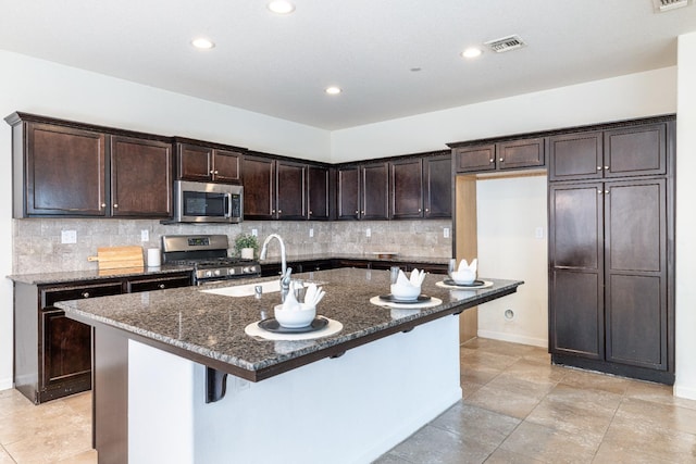 3834 Sussex Ave, Clovis, CA 93619 - kitchen with appliances with stainless steel finishes, dark stone counters, a sink, dark brown cabinetry, and tasteful backsplash