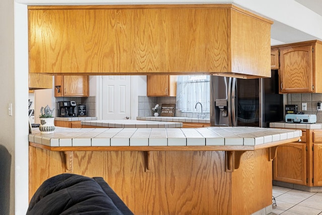 2903 Desert Ranch Way, Madera, CA 93637 - kitchen with fridge with ice dispenser, backsplash, a breakfast bar, light tile patterned flooring, and a peninsula