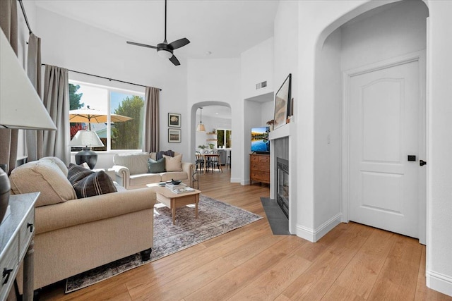 1780 N Avignon Ln, Clovis, CA 93619 - living room with arched walkways, ceiling fan, a fireplace with flush hearth, light wood-style floors, and a high ceiling