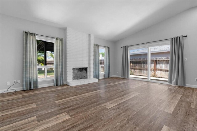 6569 N Kennedy Ave, Fresno, CA 93710 - unfurnished living room featuring vaulted ceiling, wood finished floors, a brick fireplace, and baseboards