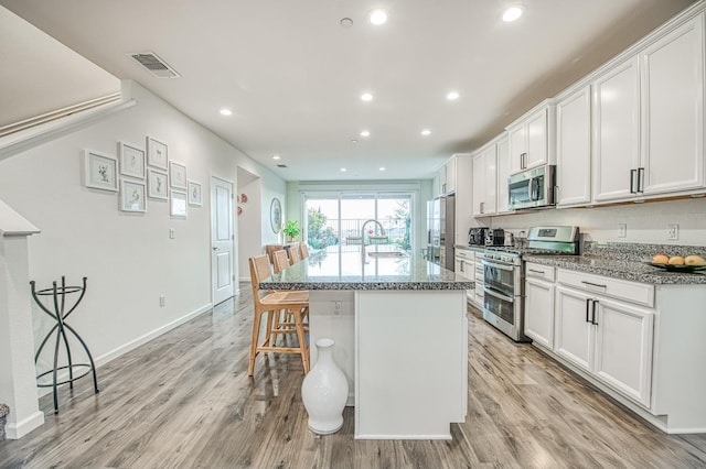 4284 Hillside Rd, Madera, CA 93636 - kitchen featuring stainless steel appliances, a sink, a center island with sink, light wood-style floors, and a kitchen bar