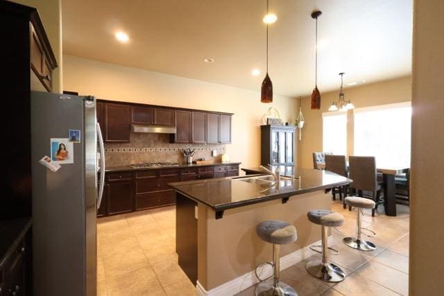 3309 Beverly Ave, Clovis, CA 93619 - kitchen with freestanding refrigerator, dark countertops, under cabinet range hood, a breakfast bar area, and a center island with sink