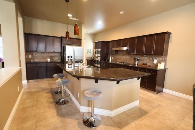 3309 Beverly Ave, Clovis, CA 93619 - kitchen featuring stainless steel appliances, light tile patterned floors, dark countertops, backsplash, and dark brown cabinetry