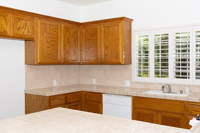 2300 Sierra Ave Unit 129, Kingsburg, CA 93631 - kitchen with dishwasher, decorative backsplash, a sink, brown cabinetry, and tile counters