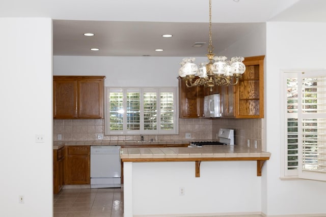 2300 Sierra Ave Unit 129, Kingsburg, CA 93631 - kitchen featuring white appliances, tile countertops, backsplash, brown cabinets, and a peninsula