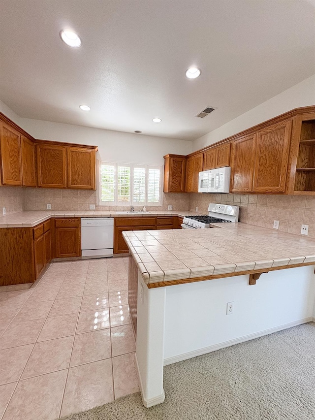 2300 Sierra Ave Unit 129, Kingsburg, CA 93631 - kitchen featuring white appliances, brown cabinetry, a peninsula, decorative backsplash, and recessed lighting