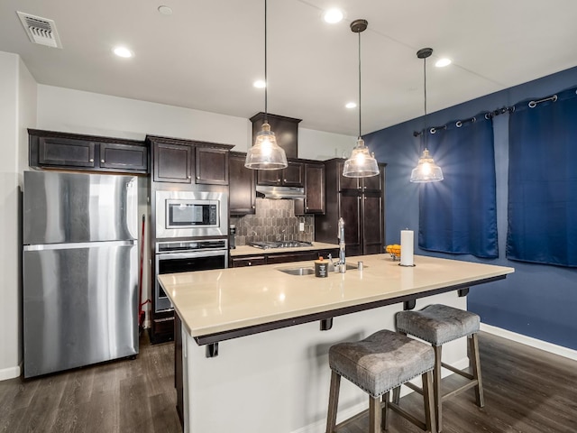 6053 E Brick Dr, Fresno, CA 93727 - kitchen featuring stainless steel appliances, dark wood-style flooring, under cabinet range hood, backsplash, and a kitchen breakfast bar