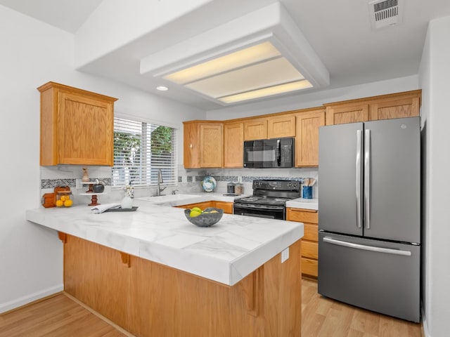 6185 N Milburn Ave, Fresno, CA 93722 - kitchen with black appliances, a sink, a peninsula, light countertops, and light wood-style flooring