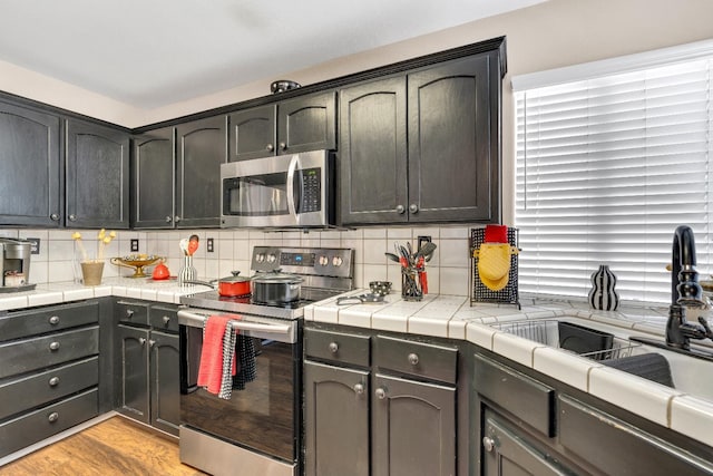 1775 E Cole Ave, Fresno, CA 93720 - kitchen featuring stainless steel appliances, decorative backsplash, a sink, light wood finished floors, and tile countertops