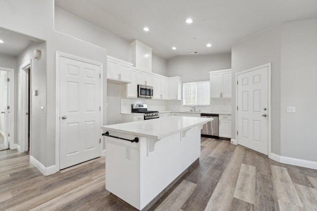 1061 Adell St, Madera, CA 93638 - kitchen with appliances with stainless steel finishes, a kitchen island, white cabinetry, tasteful backsplash, and wood finished floors