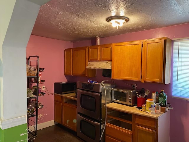1425 S 3rd St, Fresno, CA 93702 - kitchen with stainless steel double oven, a textured ceiling, light countertops, under cabinet range hood, and brown cabinetry