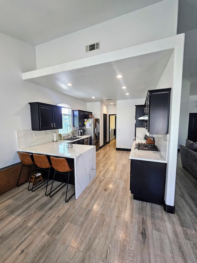 5453 N San Clemente Ave, Fresno, CA 93723 - kitchen featuring a peninsula, light wood finished floors, appliances with stainless steel finishes, a breakfast bar, and light stone countertops