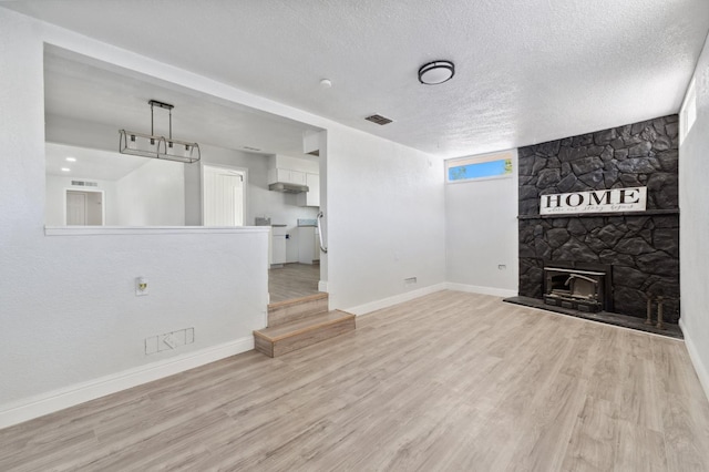 4641 E Weldon Ave, Fresno, CA 93703 - unfurnished living room with baseboards, light wood finished floors, a textured ceiling, and a stone fireplace