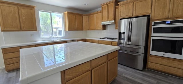 1216 Avignon Dr, Merced, CA 95348 - kitchen featuring stainless steel appliances, wood finished floors, under cabinet range hood, a sink, and decorative backsplash