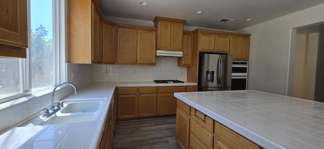 1216 Avignon Dr, Merced, CA 95348 - kitchen with appliances with stainless steel finishes, tile counters, under cabinet range hood, tasteful backsplash, and a sink