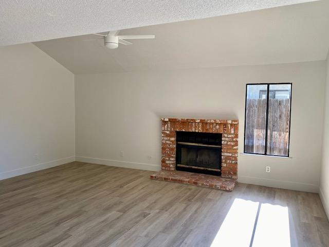 485 E Alluvial Ave Unit 102, Fresno, CA 93720 - unfurnished living room featuring a ceiling fan, wood finished floors, vaulted ceiling, a fireplace, and baseboards