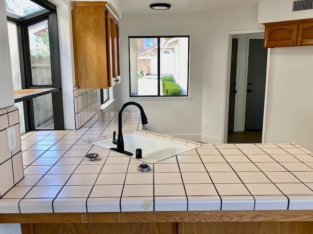 485 E Alluvial Ave Unit 102, Fresno, CA 93720 - kitchen featuring tile counters, brown cabinetry, and a peninsula
