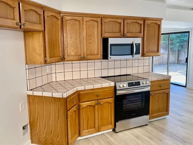 485 E Alluvial Ave Unit 102, Fresno, CA 93720 - kitchen with appliances with stainless steel finishes, tile countertops, backsplash, light wood-style floors, and brown cabinetry