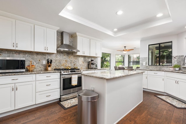 8814 N Spalding, Fresno, CA 93720 - kitchen featuring wall chimney range hood, stainless steel appliances, a tray ceiling, ornamental molding, and dark wood-style floors