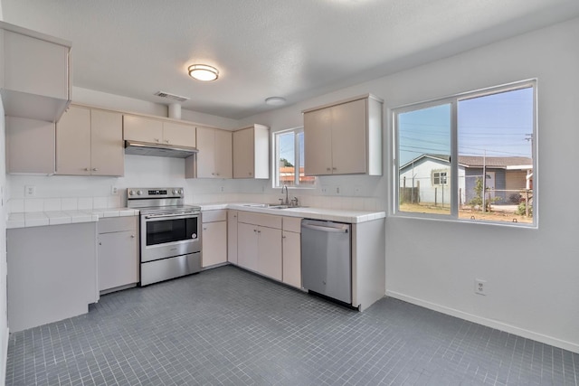 829 W Woodward Ave, Fresno, CA 93706 - kitchen with stainless steel appliances, under cabinet range hood, a sink, tile countertops, and baseboards