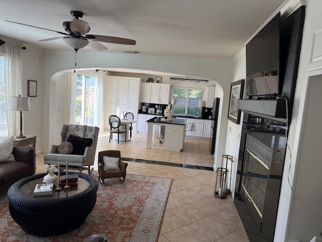 9130 Hunters Creek Way, Chowchilla, CA 93610 - living room with arched walkways, light tile patterned floors, a ceiling fan, a textured ceiling, and ornamental molding