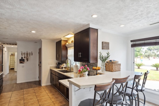 5554 E Montecito Ave, Fresno, CA 93727 - kitchen featuring a sink, light countertops, a kitchen breakfast bar, a textured ceiling, and dark brown cabinets