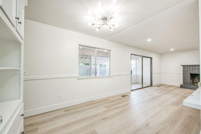1448 N Helm Ave, Fresno, CA 93727 - unfurnished living room featuring a chandelier, light wood-type flooring, a brick fireplace, baseboards, and a textured ceiling