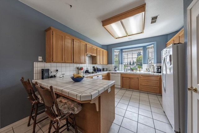 3159 Cedar Creek Ln, Madera, CA 93637 - kitchen with white appliances, a peninsula, backsplash, tile counters, and light tile patterned floors