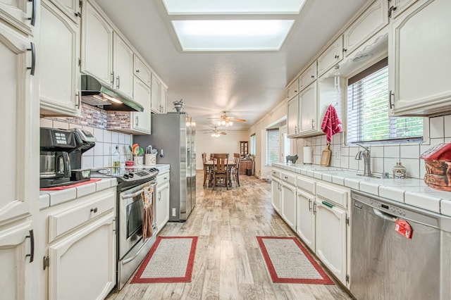1183 E Dinuba Ave, Fresno, CA 93725 - kitchen featuring stainless steel appliances, under cabinet range hood, tile countertops, backsplash, and plenty of natural light