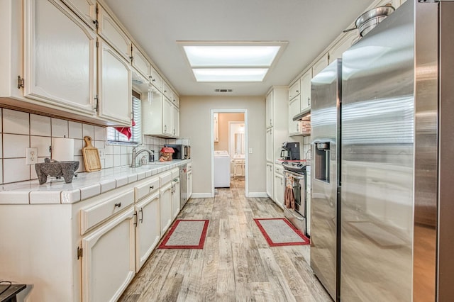 1183 E Dinuba Ave, Fresno, CA 93725 - kitchen featuring stainless steel appliances, washer / dryer, light wood-type flooring, a sink, and decorative backsplash
