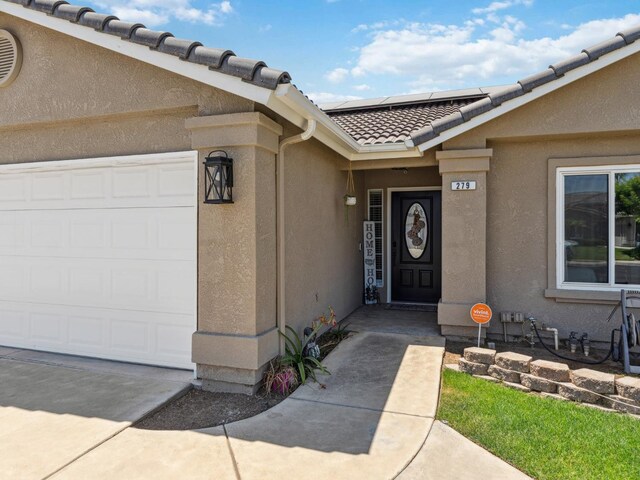 279 Lily Ave, Sanger, CA 93657 - view of exterior entry featuring a tiled roof, a garage, stucco siding, and solar panels