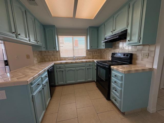 2407 W Carmen Ave, Fresno, CA 93728 - kitchen with black appliances, under cabinet range hood, tile counters, backsplash, and light tile patterned flooring