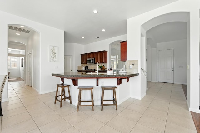 2721 Stuart Ave, Clovis, CA 93611 - kitchen with stainless steel microwave, light tile patterned floors, a breakfast bar, a peninsula, and baseboards