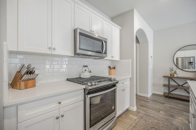 6085 E Homan Ave, Fresno, CA 93727 - kitchen with stainless steel appliances, light wood finished floors, tasteful backsplash, white cabinets, and arched walkways
