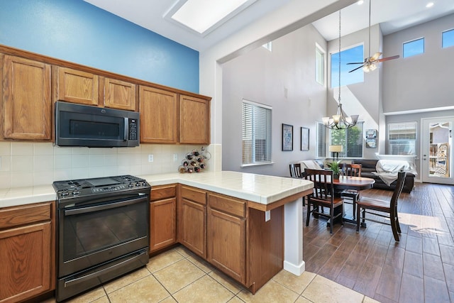 73 W Bordeaux Ln, Clovis, CA 93619 - kitchen featuring black appliances, a towering ceiling, a peninsula, brown cabinetry, and a ceiling fan