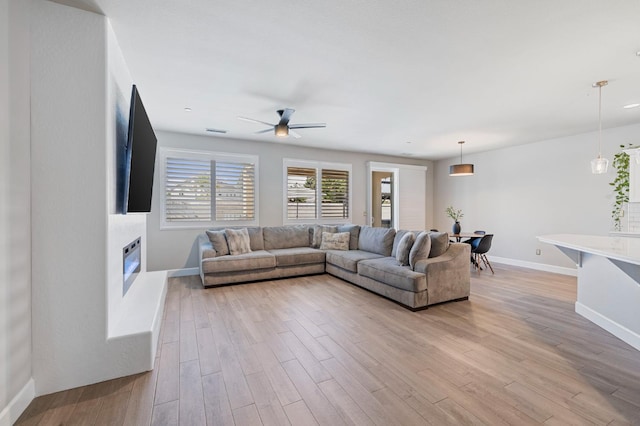 7374 E Flint Way, Fresno, CA 93737 - living area with a glass covered fireplace, light wood-style flooring, ceiling fan, and baseboards