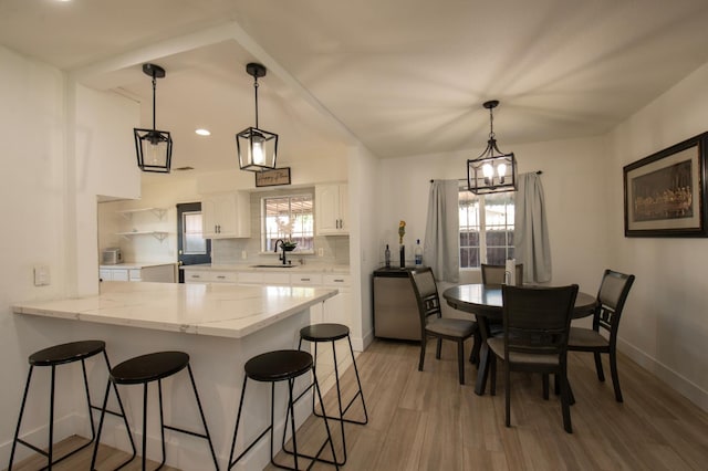 168 E Stuart Ave, Fresno, CA 93710 - kitchen with a sink, a kitchen bar, white cabinetry, a peninsula, and light wood-style flooring